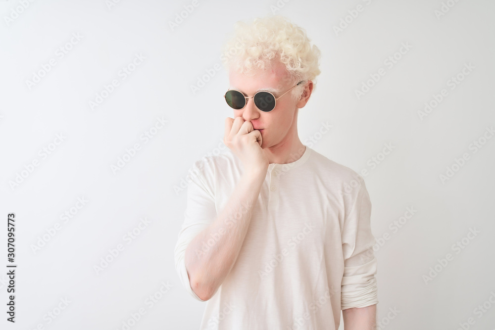 Young albino blond man wearing t-shirt and sunglasses over isolated white background looking stressed and nervous with hands on mouth biting nails. Anxiety problem.