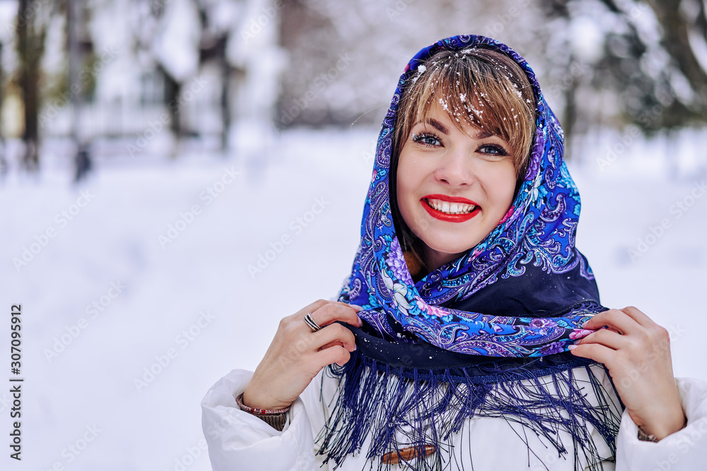 portrait of a cute young woman in a blue national scarf in winter on nature.the girl smiles broadly portrait of a cute young woman in a blue national scarf in winter on nature.the girl smiles broadly