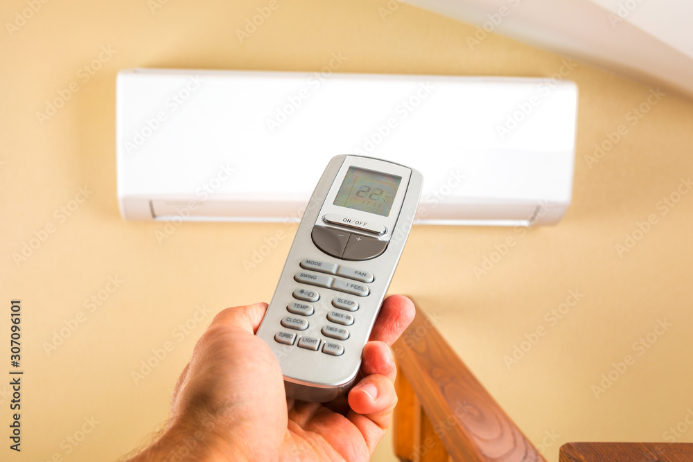 Hand with remote control directed on the conditioner on the wall Hand with remote control directed on the conditioner on the wall