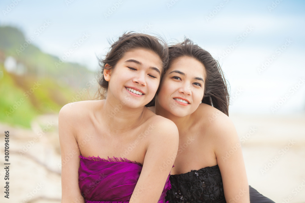 Two teen girls in elegant dresses smiling together on beach