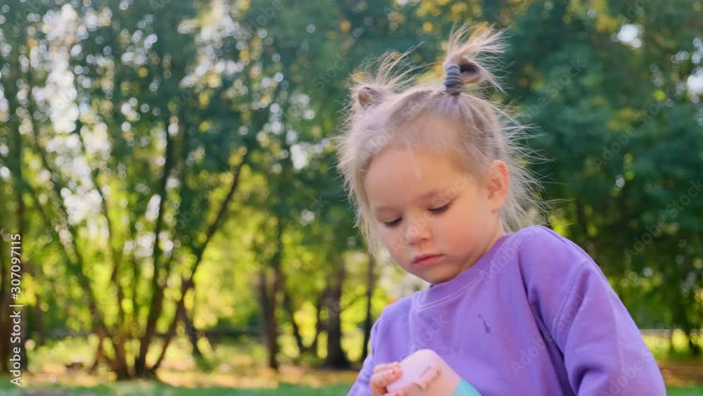 A little girl in a park holds a thermos in her hands. She wants to drink from a metal bottle A little girl in a park holds a thermos in her hands. She wants to drink from a metal bottle