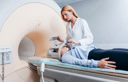 Radiologic blonde model technician help at mature female patient lying on a CT Scan bed