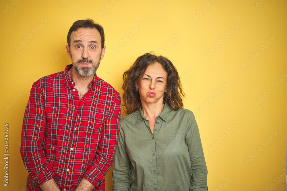 Beautiful middle age couple over isolated yellow background puffing cheeks with funny face. Mouth inflated with air, crazy expression. Beautiful middle age couple over isolated yellow background puffing cheeks with funny face. Mouth inflated with air, crazy expression.