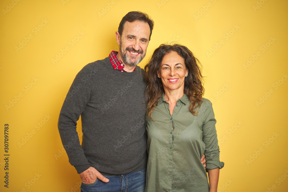 Beautiful middle age couple over isolated yellow background with a happy and cool smile on face. Lucky person. Beautiful middle age couple over isolated yellow background with a happy and cool smile on face. Lucky person.