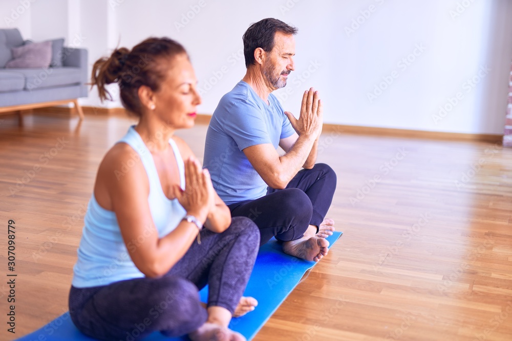 Middle age beautiful sporty couple sitting on mat practicing yoga doing prayer pose at gym Middle age beautiful sporty couple sitting on mat practicing yoga doing prayer pose at gym