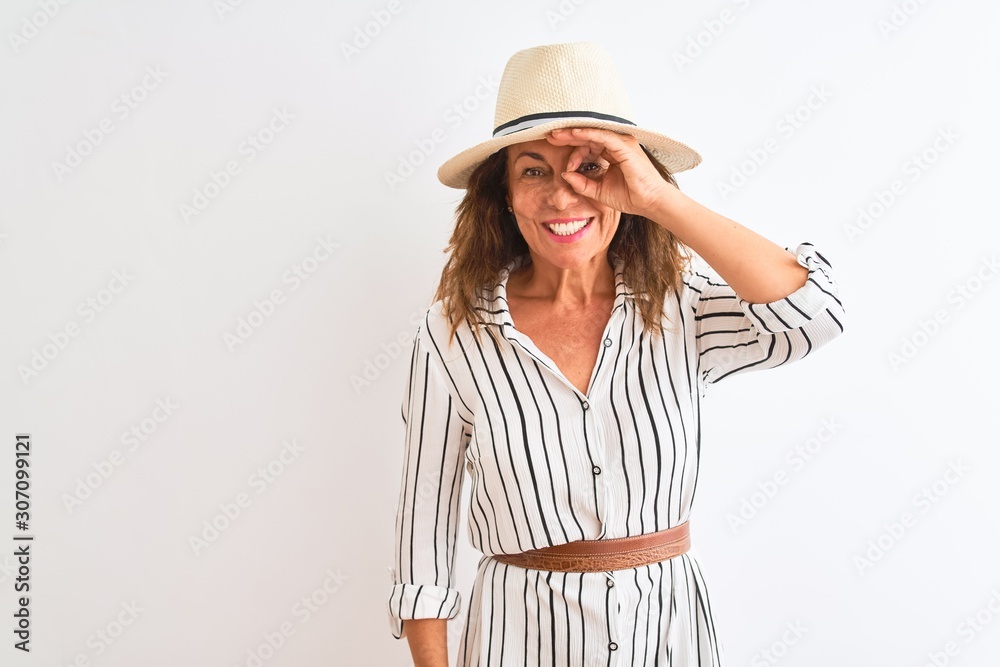 Middle age businesswoman wearing striped dress and hat over isolated white background doing ok gesture with hand smiling, eye looking through fingers with happy face. Middle age businesswoman wearing striped dress and hat over isolated white background doing ok gesture with hand smiling, eye looking through fingers with happy face.