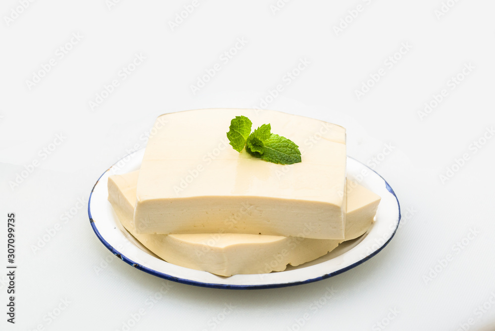 Two pieces of tofu served on a plate with green mint leaves on a white background