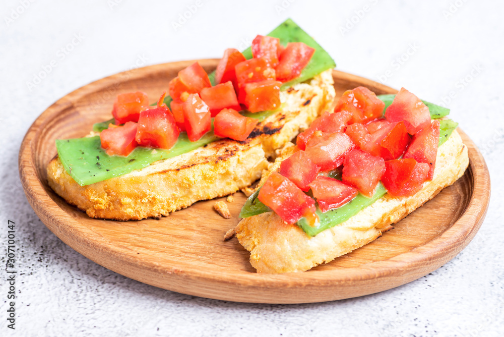 two Italian bruschettes with cheese and tomatoes on a wooden plate two Italian bruschettes with cheese and tomatoes on a wooden plate