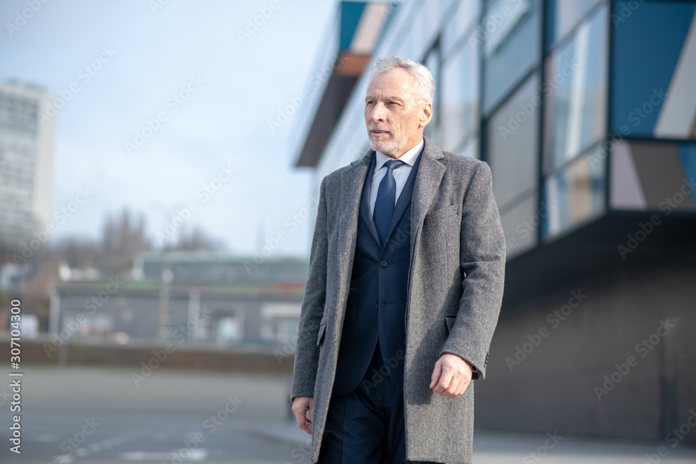 Grey-haired man wearing a grey coat standing near the office Grey-haired man wearing a grey coat standing near the office