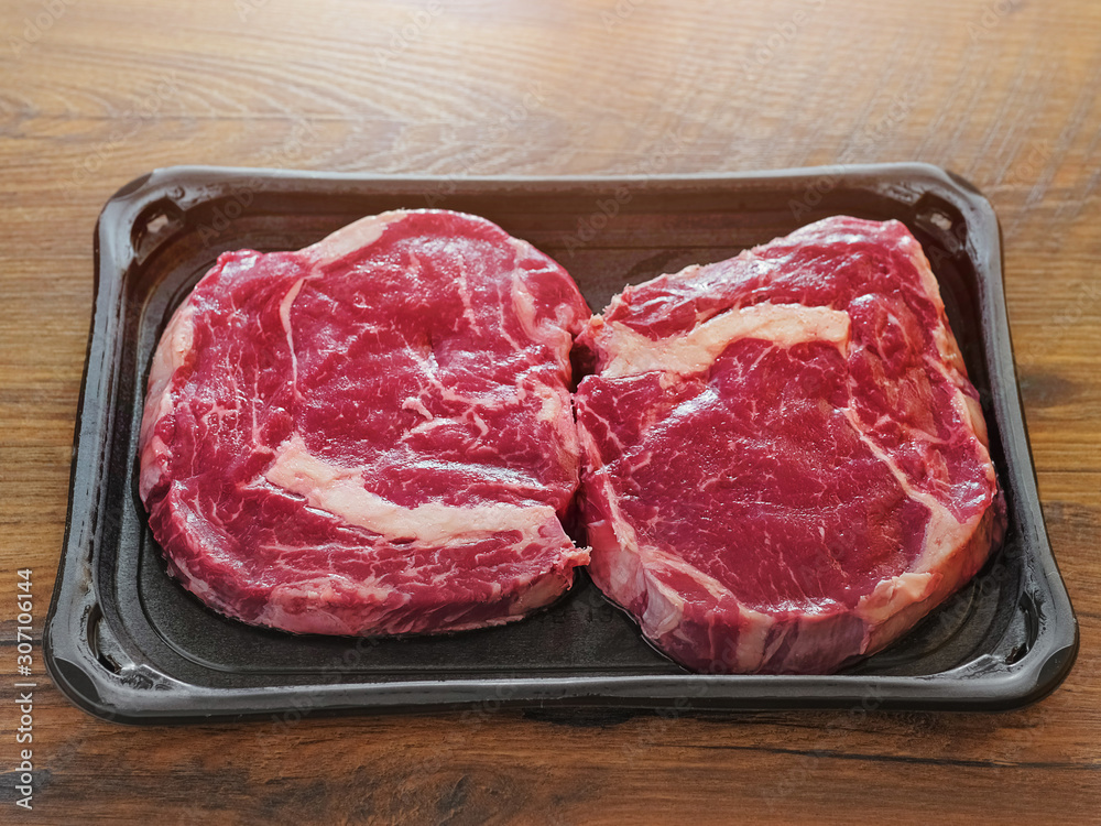 Two raw uncooked premium fresh rib eye steaks on a plastic tray, Top quailty product from supermarket. On a wooden table.