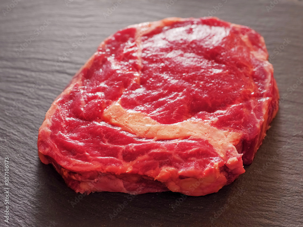 Fototapeta premium Fresh and juicy uncooked rib eye steak, premium cut of beef. On a stone surface, selective focus.