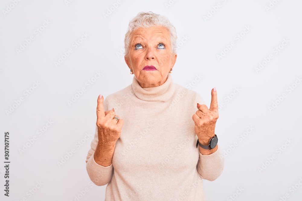 Senior grey-haired woman wearing turtleneck sweater standing over isolated white background Pointing up looking sad and upset, indicating direction with fingers, unhappy and depressed. Senior grey-haired woman wearing turtleneck sweater standing over isolated white background Pointing up looking sad and upset, indicating direction with fingers, unhappy and depressed.