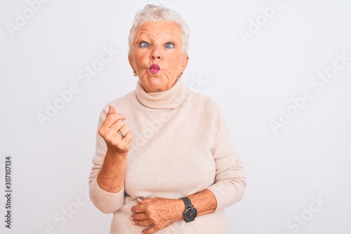 Senior grey-haired woman wearing turtleneck sweater standing over isolated white background making fish face with lips, crazy and comical gesture. Funny expression.