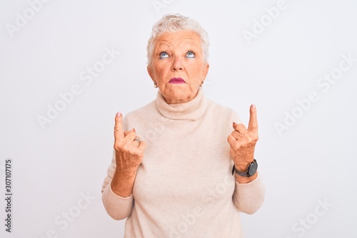 Senior grey-haired woman wearing turtleneck sweater standing over isolated white background Pointing up looking sad and upset, indicating direction with fingers, unhappy and depressed.