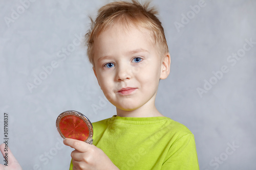 Cute little caucasian boy looks to hand mirror smiling. Blond hair, bright blue eyes, pretty child admires himself. Children diversity concept. Indoors, copy space. photo