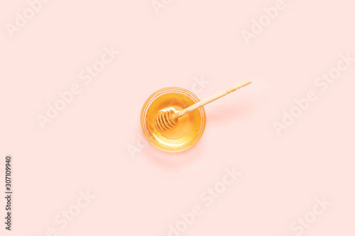 Fresh honey in glass bowl with wooden spoon on pink background, top view