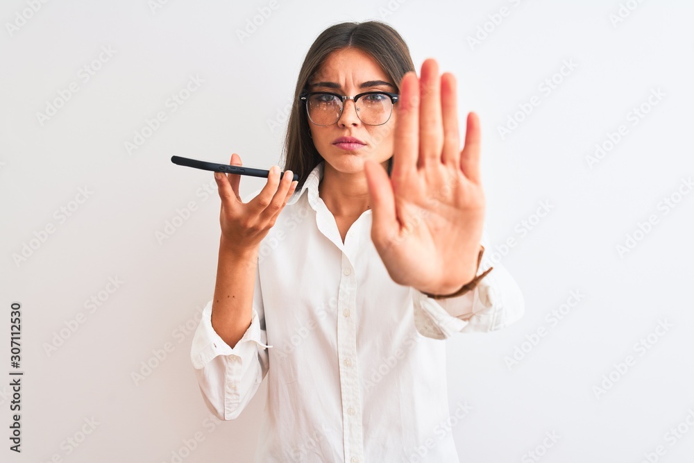 Woman wearing glasses sending message on smartphone over isolated white background with open hand doing stop sign with serious and confident expression, defense gesture Woman wearing glasses sending message on smartphone over isolated white background with open hand doing stop sign with serious and confident expression, defense gesture