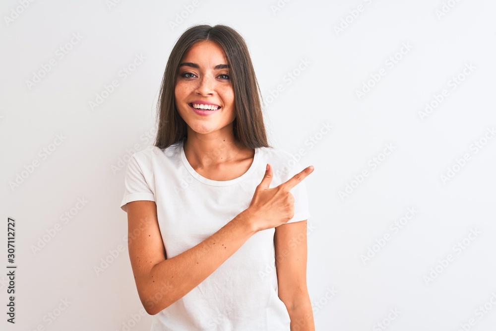 Young beautiful woman wearing casual t-shirt standing over isolated white background cheerful with a smile on face pointing with hand and finger up to the side with happy and natural expression Young beautiful woman wearing casual t-shirt standing over isolated white background cheerful with a smile on face pointing with hand and finger up to the side with happy and natural expression