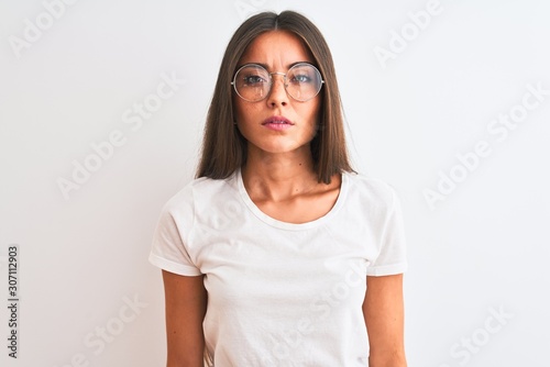 Young beautiful woman wearing casual t-shirt and glasses over isolated white background with serious expression on face. Simple and natural looking at the camera. © Krakenimages.com