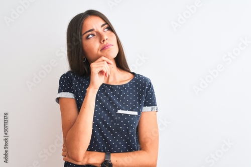 Young beautiful woman wearing blue casual t-shirt standing over isolated white background with hand on chin thinking about question, pensive expression. Smiling with thoughtful face. Doubt concept.