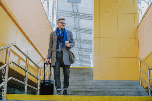 Handsome young man carrying travel suitcase and smiling