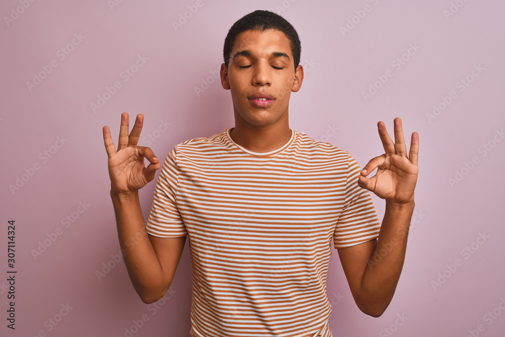 Young handsome arab man wearing striped t-shirt standing over isolated pink background relax and smiling with eyes closed doing meditation gesture with fingers. Yoga concept. Young handsome arab man wearing striped t-shirt standing over isolated pink background relax and smiling with eyes closed doing meditation gesture with fingers. Yoga concept.