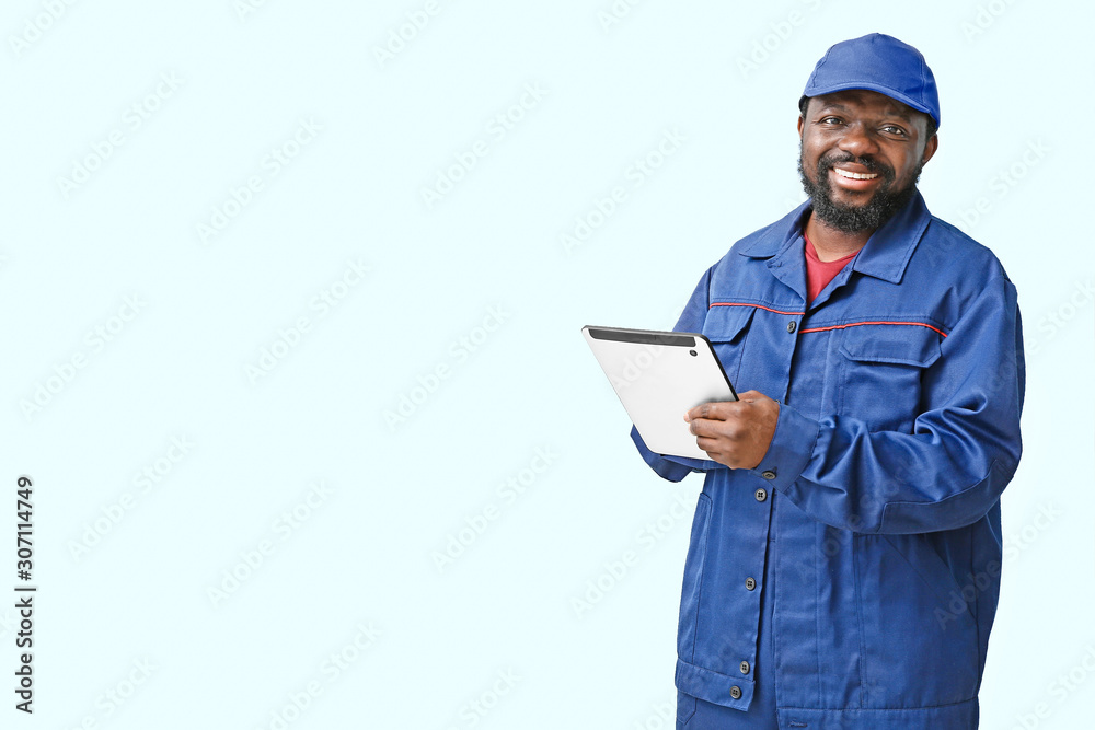 African-American car mechanic with tablet computer on light background African-American car mechanic with tablet computer on light background