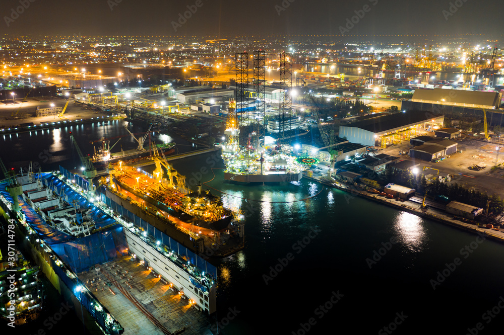 Obraz premium Aerial view of a jack up oil drilling rig and dry dock ship in the shipyard for maintenance during suset time.