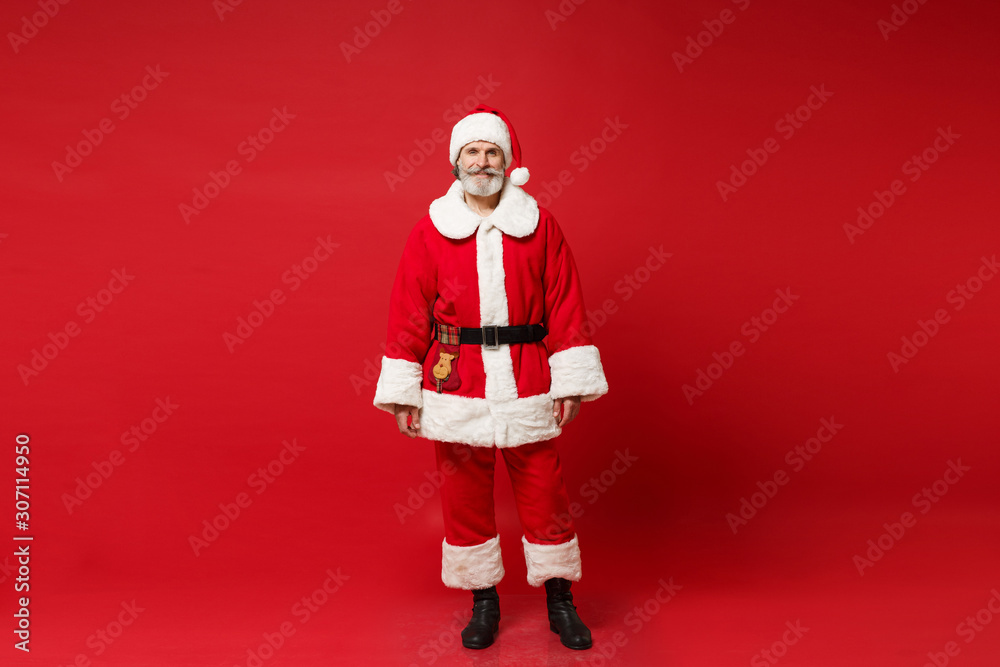Smiling elderly gray-haired mustache bearded Santa man in Christmas hat posing isolated on red wall background, studio portrait. Happy New Year 2020 celebration holiday concept. Mock up copy space. Smiling elderly gray-haired mustache bearded Santa man in Christmas hat posing isolated on red wall background, studio portrait. Happy New Year 2020 celebration holiday concept. Mock up copy space.