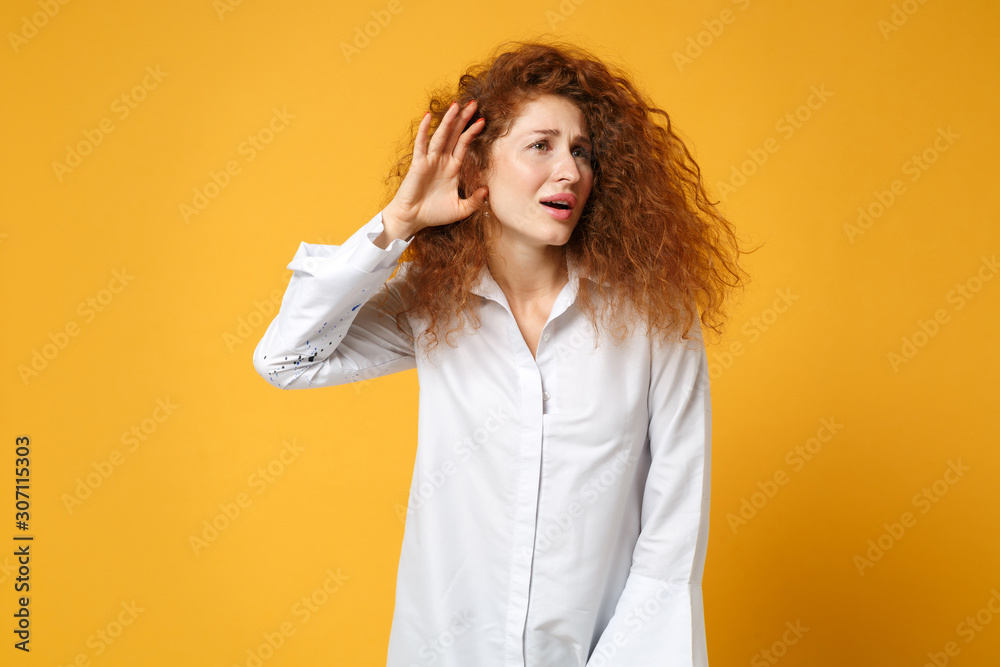 Young redhead woman girl in casual white shirt posing isolated on yellow orange background in studio. People sincere emotions lifestyle concept. Mock up copy space. Try hear you with hand near ear. Young redhead woman girl in casual white shirt posing isolated on yellow orange background in studio. People sincere emotions lifestyle concept. Mock up copy space. Try hear you with hand near ear.