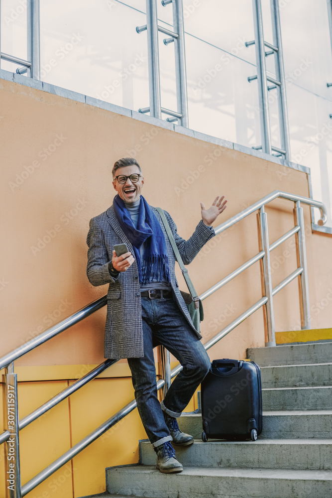 Happy stylish man with cellphone standing on staircase
