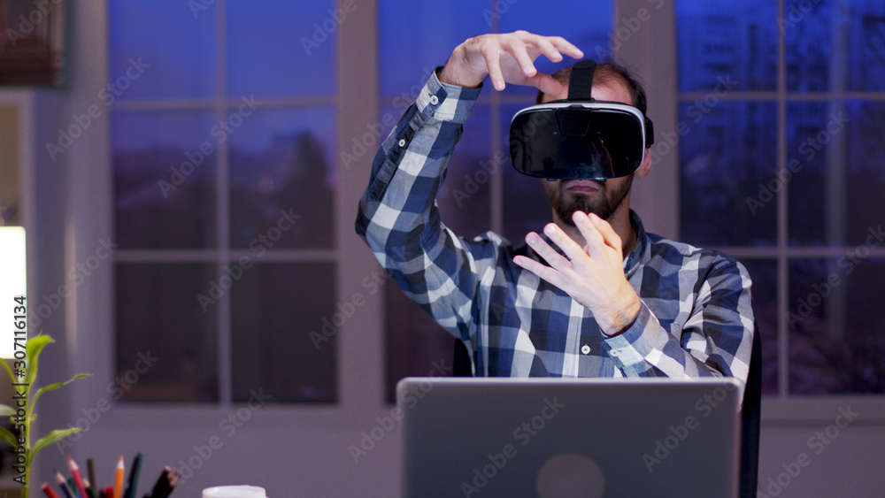 Young businessman using virtual reality goggles at night in his home office Young businessman using virtual reality goggles at night in his home office