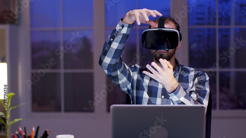 Young businessman using virtual reality goggles at night in his home office