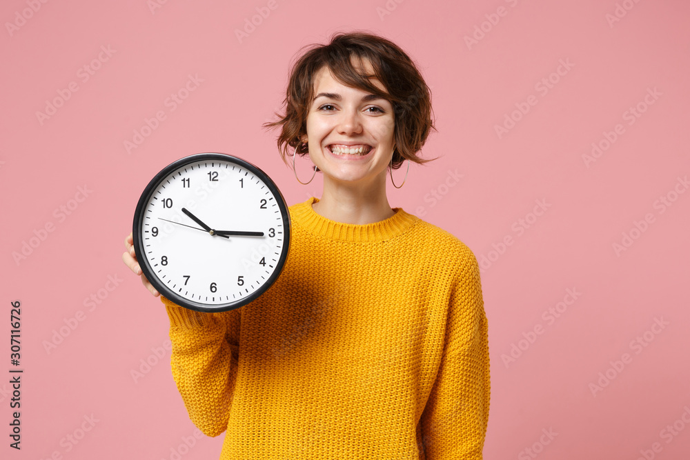 Cheerful young brunette woman girl in yellow sweater posing isolated on pastel pink wall background, studio portrait. People sincere emotions lifestyle concept. Mock up copy space. Hold in hand clock. Cheerful young brunette woman girl in yellow sweater posing isolated on pastel pink wall background, studio portrait. People sincere emotions lifestyle concept. Mock up copy space. Hold in hand clock.
