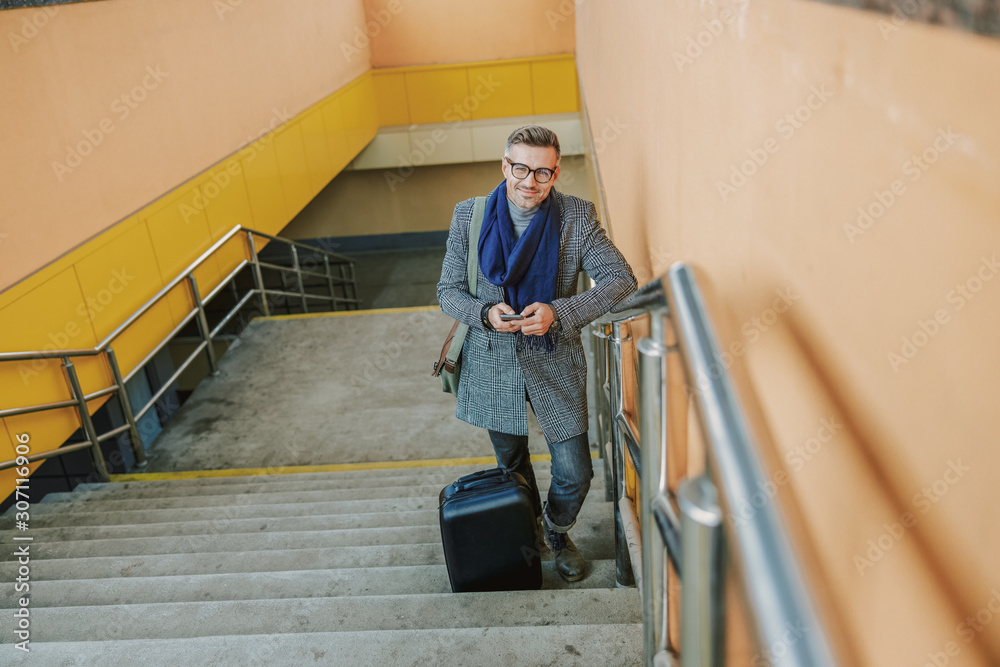 Handsome joyful man standing on steps and using cellphone