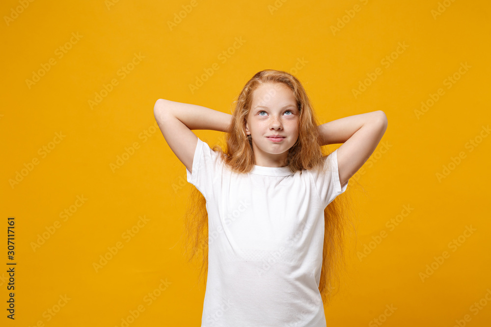Pensive little ginger kid girl 12-13 years old in white t-shirt isolated on yellow background children portrait. Childhood lifestyle concept. Mock up copy space. Looking up with hands behind head.