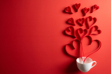 Red paper hearts splash out from white coffee cup on red paper background. Love and Valentine's day concept.