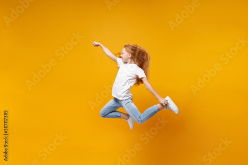 Side view of little ginger kid girl 12-13 years old in white t-shirt isolated on yellow background children portrait. Childhood lifestyle concept. Mock up copy space. Having fun, fooling around, jump.
