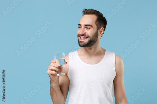 Bearded young man 20s years old perfect skin in white shirt hold water isolated on blue pastel wall background, studio portrait. Skin care healthcare cosmetic procedures concept. Mock up copy space.