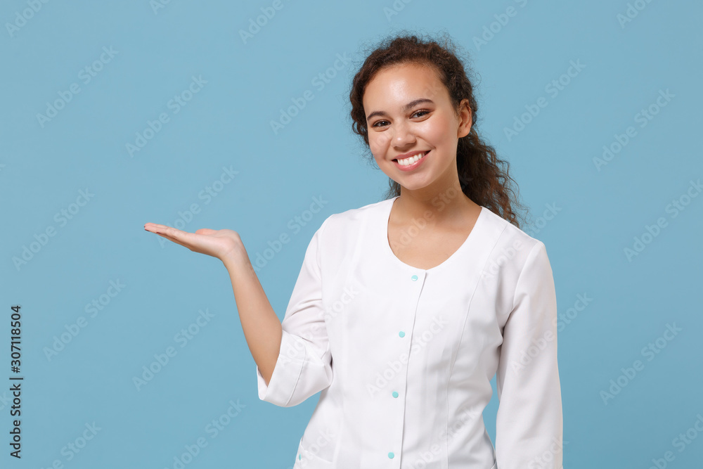 Smiling african american doctor woman isolated on blue background in studio. Female doctor in white medical gown pointing hand aside. Healthcare personnel health medicine concept. Mock up copy space. Smiling african american doctor woman isolated on blue background in studio. Female doctor in white medical gown pointing hand aside. Healthcare personnel health medicine concept. Mock up copy space.