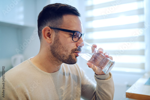 Valokuva Side view of beautiful caucasian man sitting at dining table and drinking water