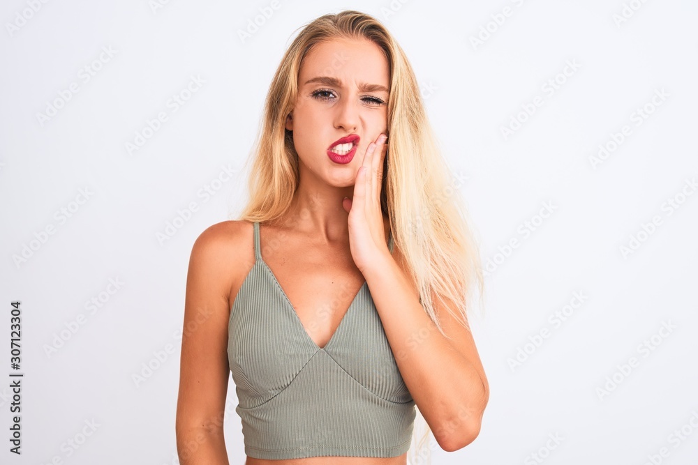 Young beautiful woman wearing casual green t-shirt standing over isolated white background touching mouth with hand with painful expression because of toothache or dental illness on teeth. Young beautiful woman wearing casual green t-shirt standing over isolated white background touching mouth with hand with painful expression because of toothache or dental illness on teeth.