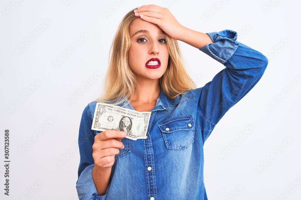 Young beautiful blond woman holding dollar standing over isolated white background stressed with hand on head, shocked with shame and surprise face, angry and frustrated. Fear and upset for mistake. Young beautiful blond woman holding dollar standing over isolated white background stressed with hand on head, shocked with shame and surprise face, angry and frustrated. Fear and upset for mistake.