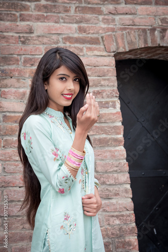 Smiling ethnic girl, hand in traditional indian mudra gesture stand. Girl in traditional Indian clothing, salwar kameez.  Indian girl in traditional dress stand at the entrance to the house.	 photo