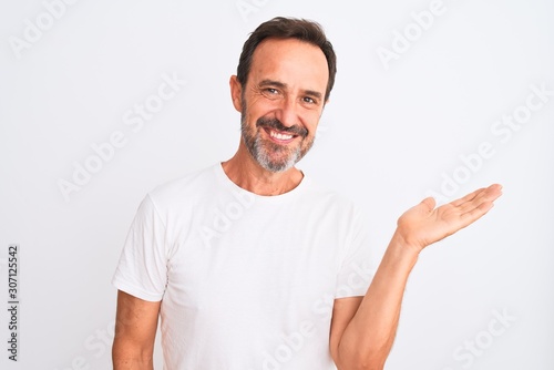 Middle age handsome man wearing casual t-shirt standing over isolated white background smiling cheerful presenting and pointing with palm of hand looking at the camera.