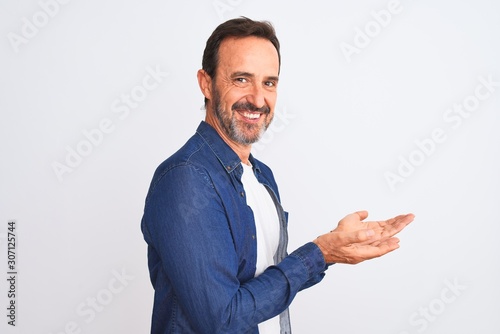 Middle age handsome man wearing blue denim shirt standing over isolated white background pointing aside with hands open palms showing copy space, presenting advertisement smiling excited happy