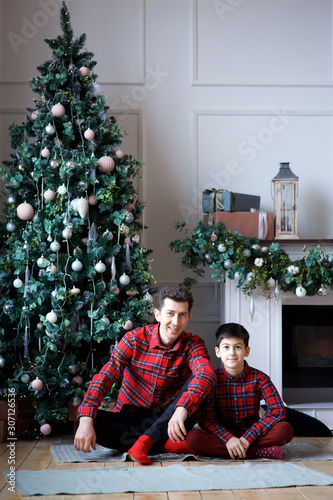 A young dad and his son in festive attire are in a room decorated for the New year and Christmas. * © Fotoproff