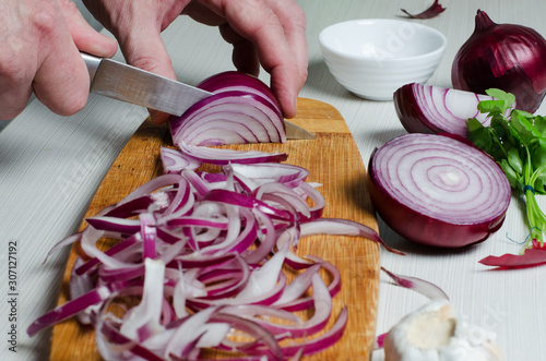 A man cuts red onions on a wooden chopping Board with a kitchen knife. Hands close up. Preparing food. Side view photo