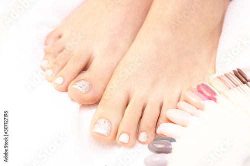 Female legs and varnish testers on a white background. Nails get a fresh and neat look during the pedicure procedure. Close up of female legs in spa salon.