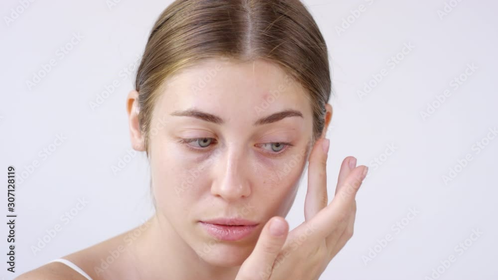 Close up shot with grey background. Beautiful woman with no makeup on applying moisturizing cream under her eyes